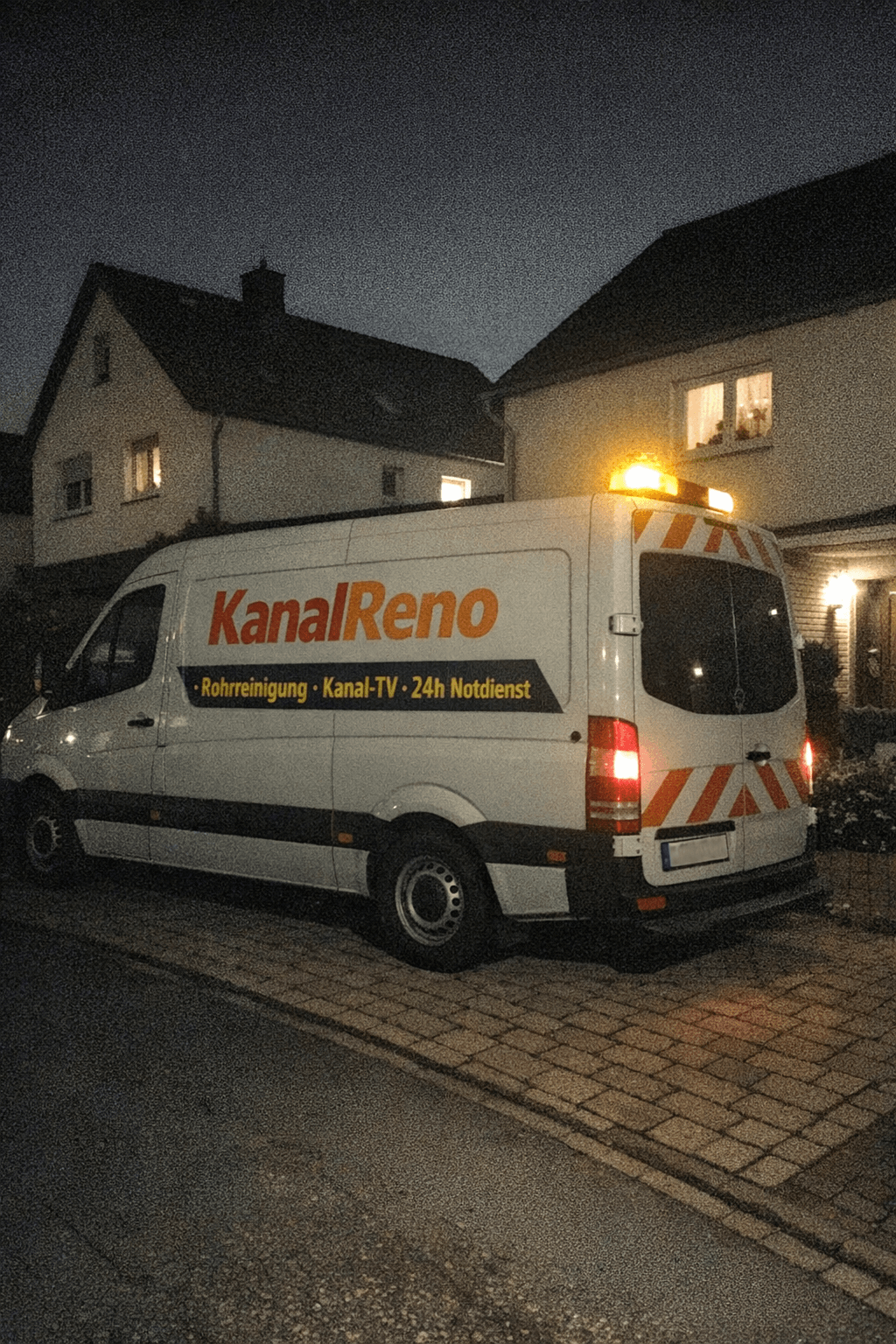 Notdienstfahrzeug steht mit Warnblinker vor einem Reihenhaus, nasse Straße spiegelt die Scheinwerfer